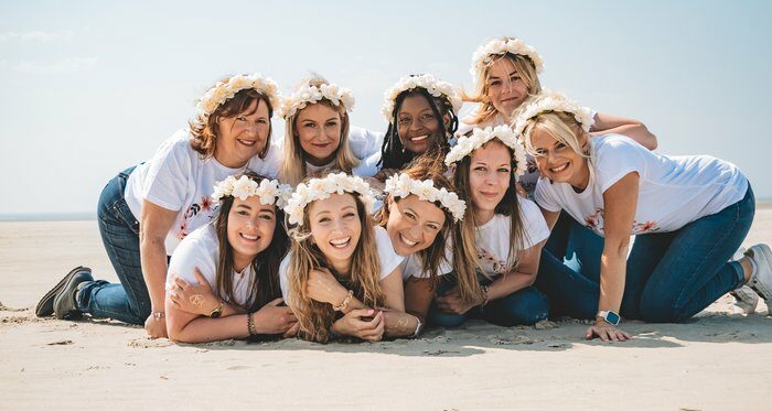 Groupe de filles posant allongées sur la plage pour un enterrement de vie de jeune fille à La Rochelle, toutes souriantes avec des couronnes de fleurs blanches