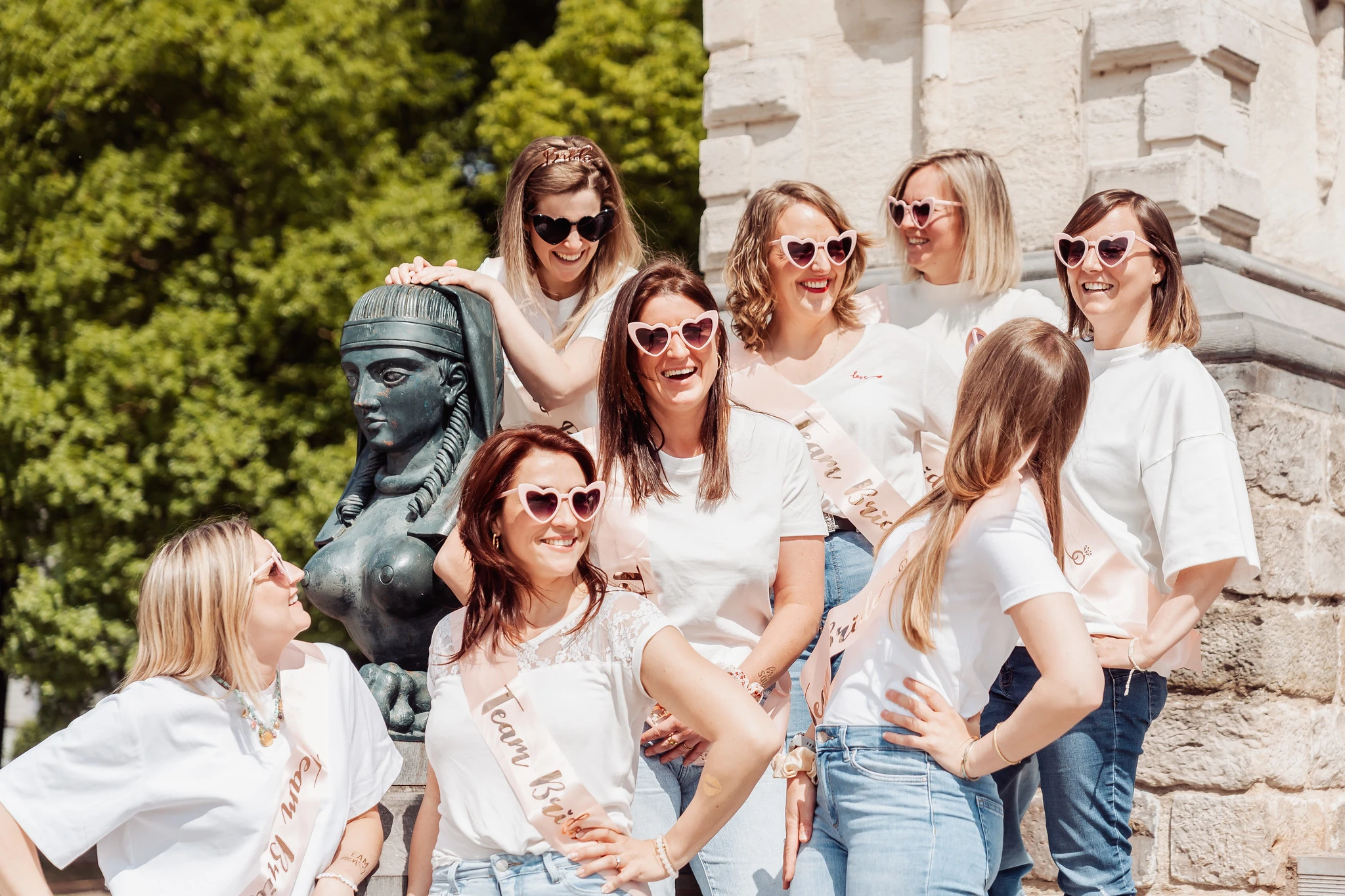 EVJF Lille – Rires et complicité autour d'une statue égyptienne Groupe de copines en t-shirts et écharpes EVJF roses autour d’une statue à Lille en pleine séance photo