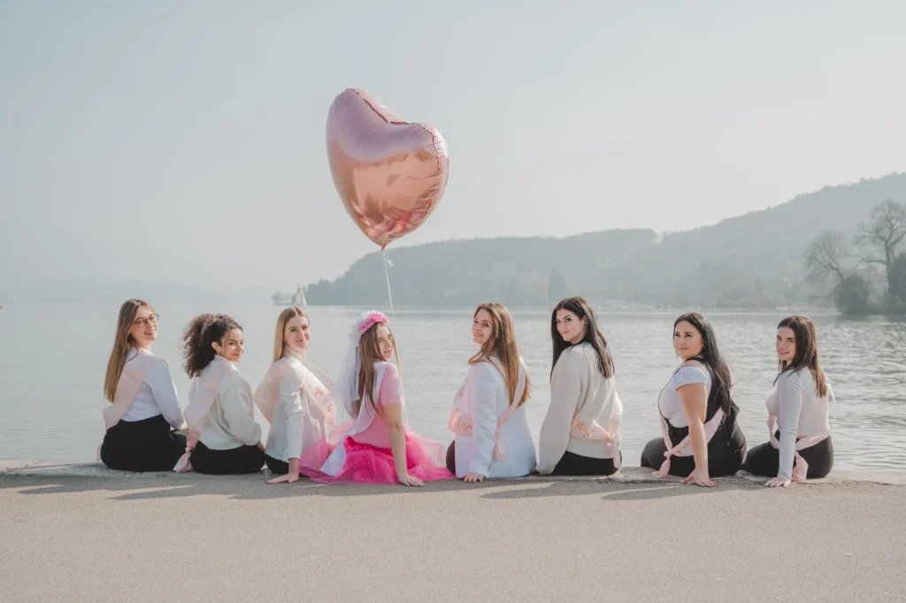 meilleures activités evjf annecy - accessoires evjf L'équipe de la mariée assise au bord du lac avec un ballon cœur rose
