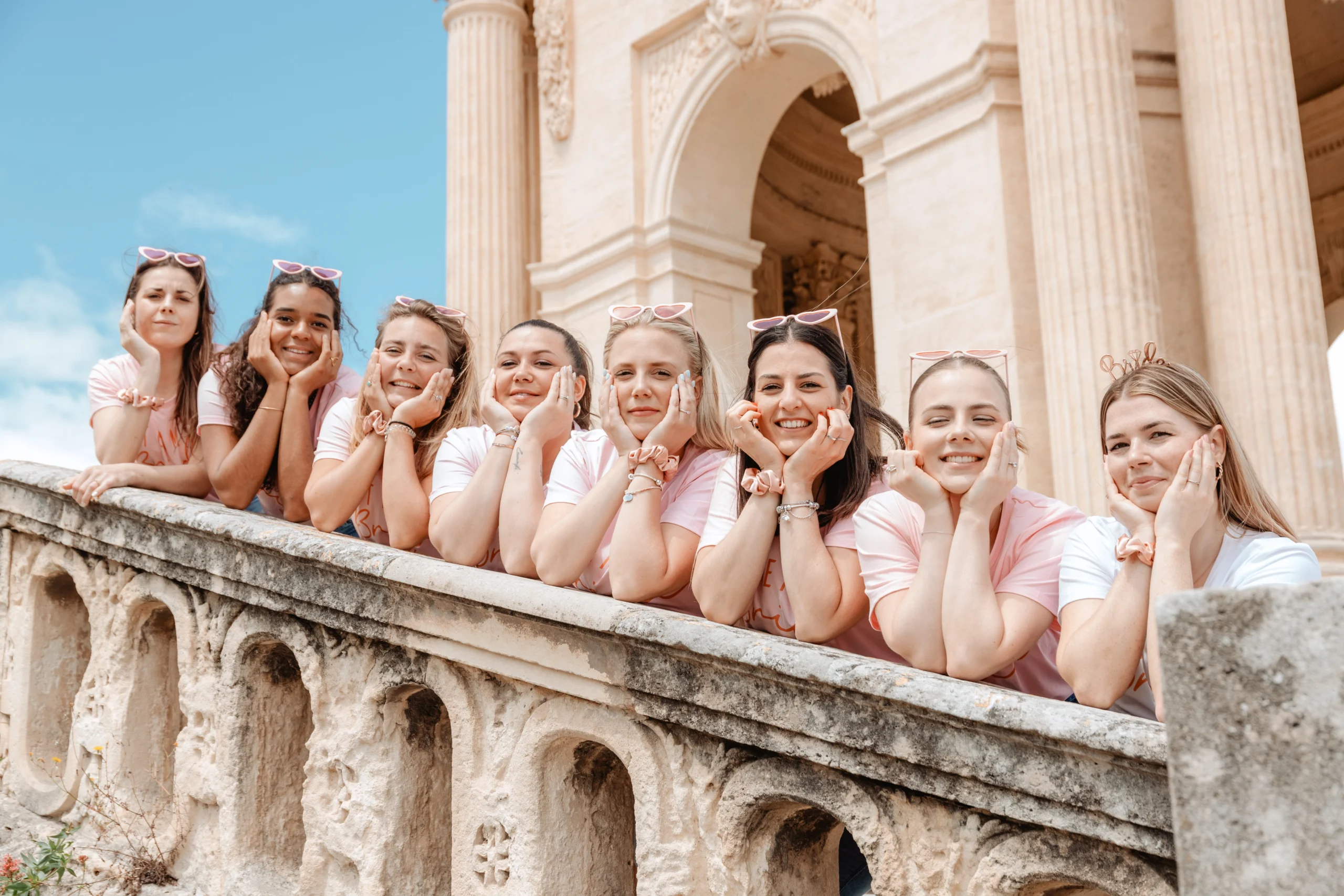 Groupe de filles souriantes en t-shirts assortis posant devant des colonnes historiques lors d’un EVJF à Barcelone