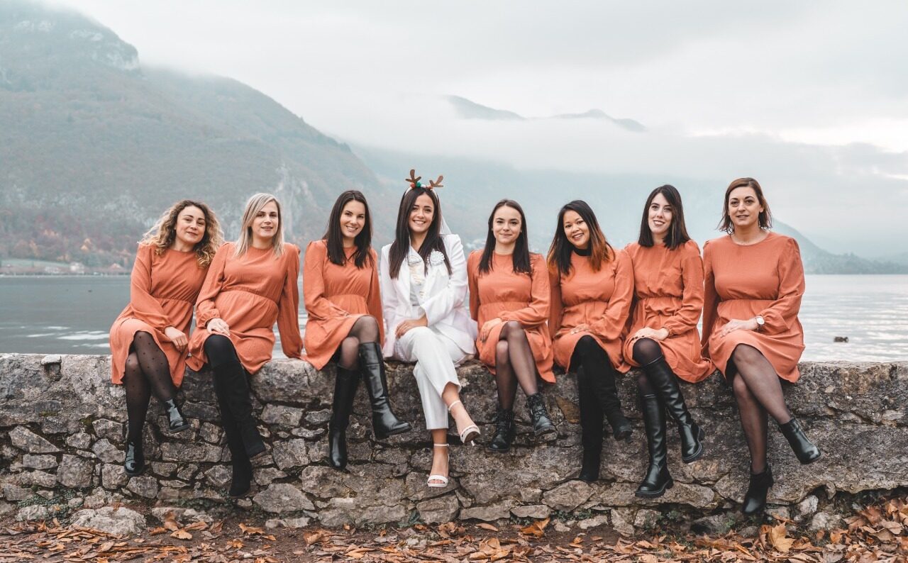 Photo EVJF à Chambéry sur un ponton au bord du lac, avec toutes les participantes en robe orange et la mariée en blanc