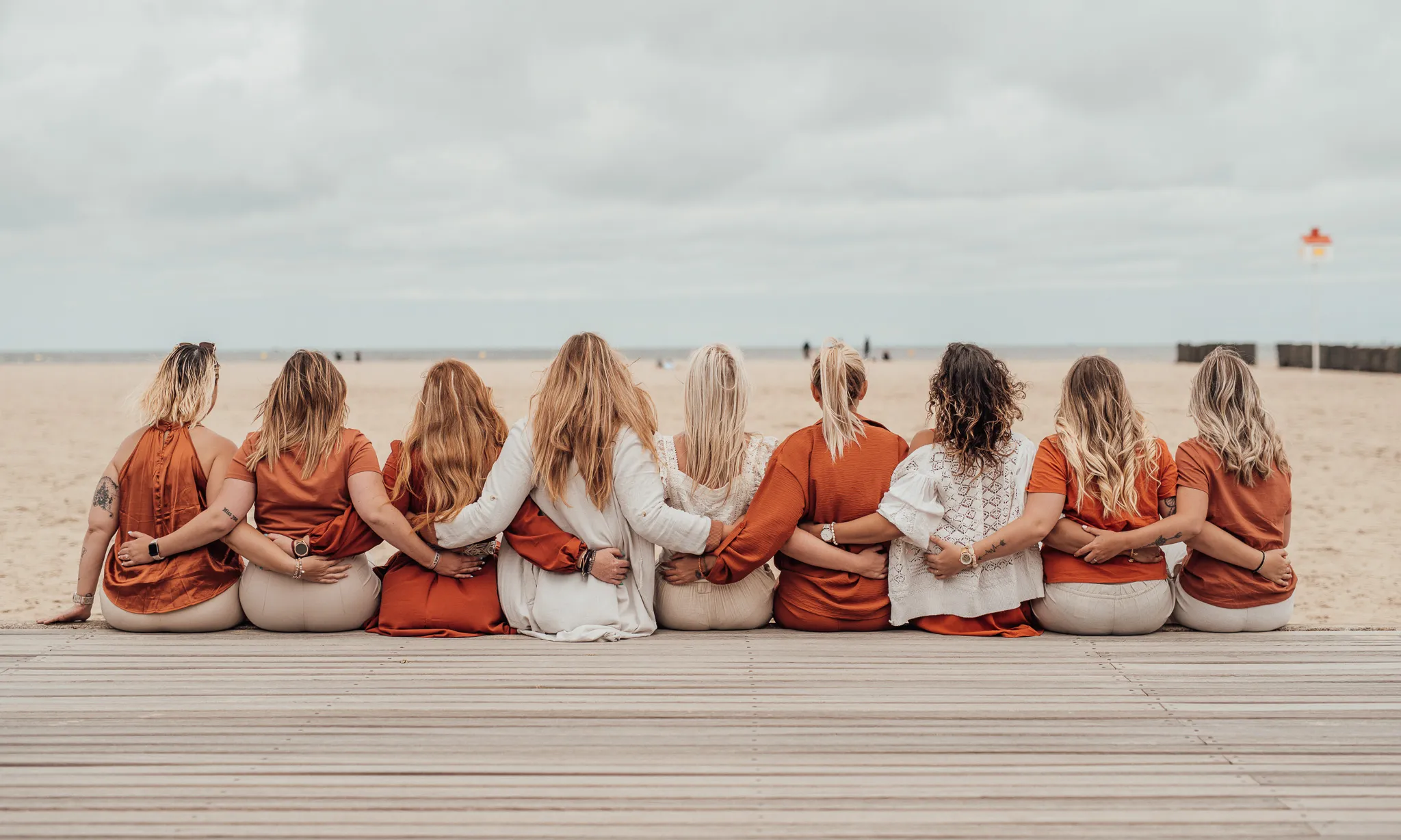 evjf-deauville-dos-groupe-orange EVJF à Deauville – Photo de groupe de dos, tenues coordonnées orange et beige face à la mer