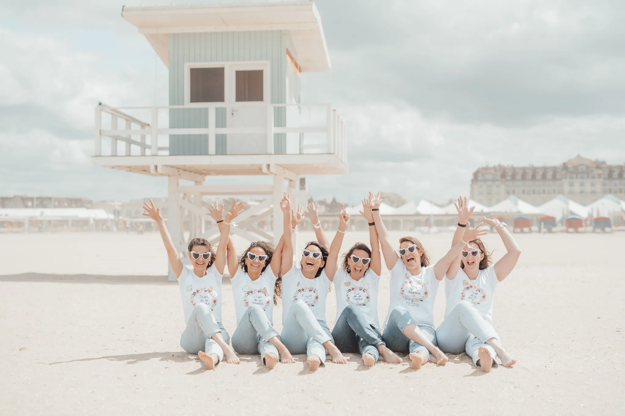 EVJF à Deauville – Groupe de copines avec lunettes cœur sur la plage devant une cabane, ambiance festive et estivale