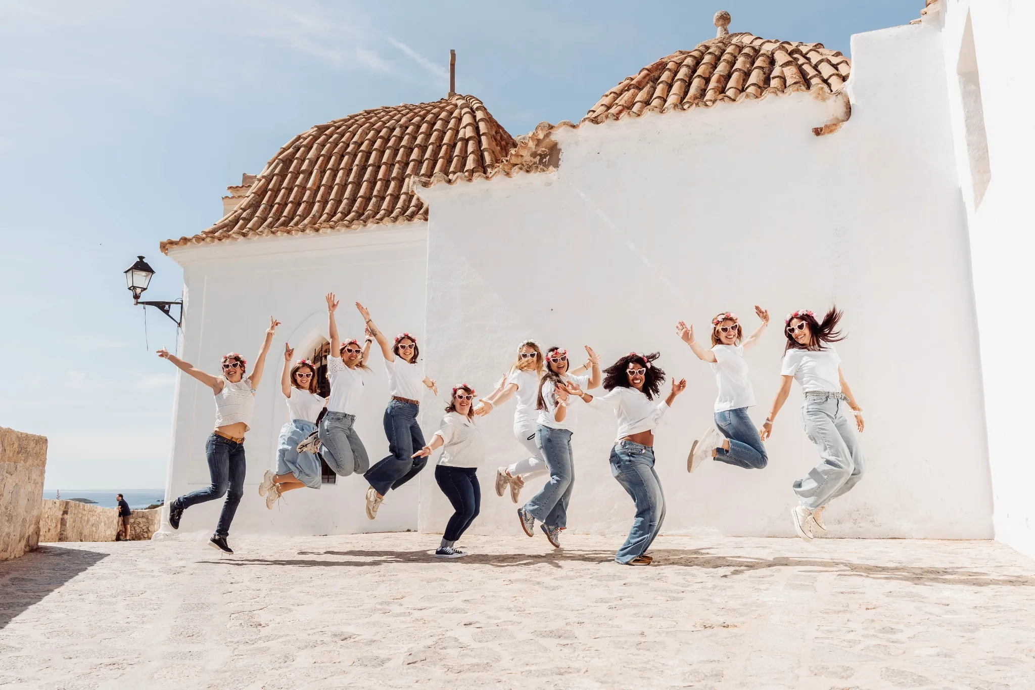 evjf-ibiza-groupe-saut-ruelles Photo de groupe EVJF à Ibiza sautant en l'air dans une ruelle ensoleillée