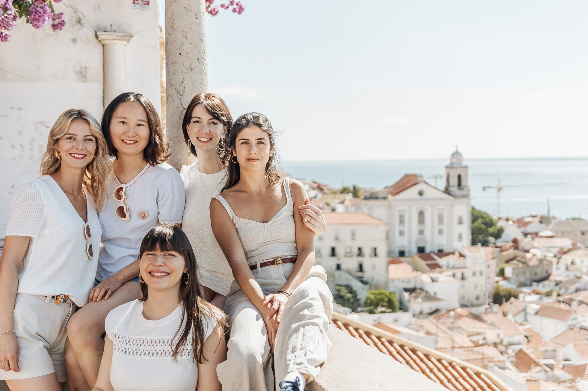 Groupe de femmes souriantes lors d’un EVJF à Lisbonne, posant en haut d’un belvédère du quartier de l’Alfama avec vue panoramique sur les toits et l’océan.