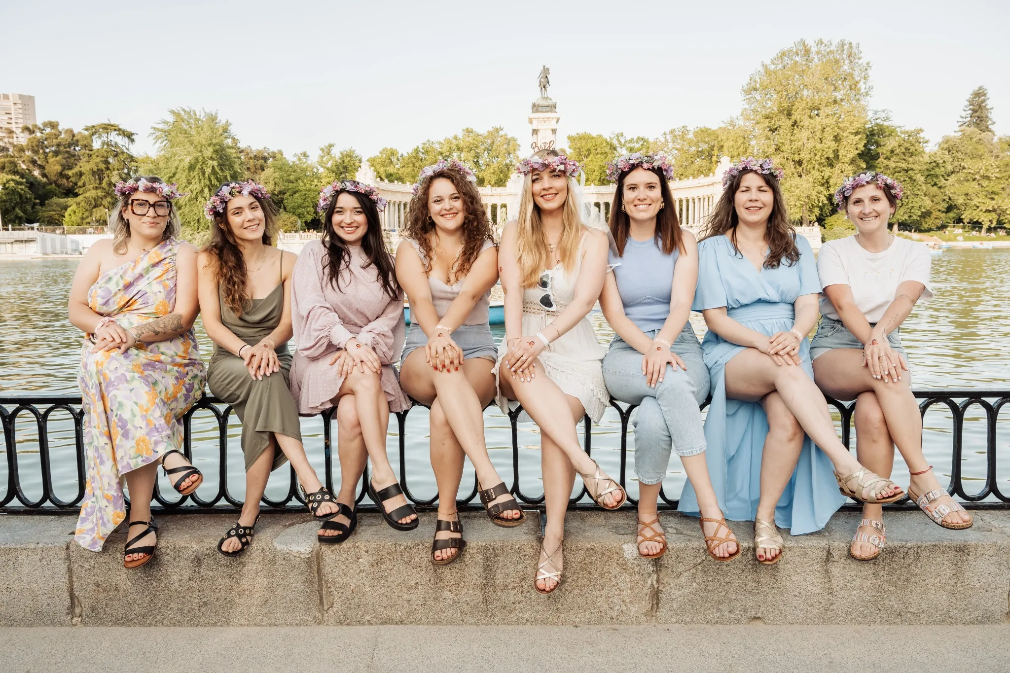 Participants d’un EVJF assises en ligne au bord du lac du parc du Retiro à Madrid, portant des couronnes de fleurs