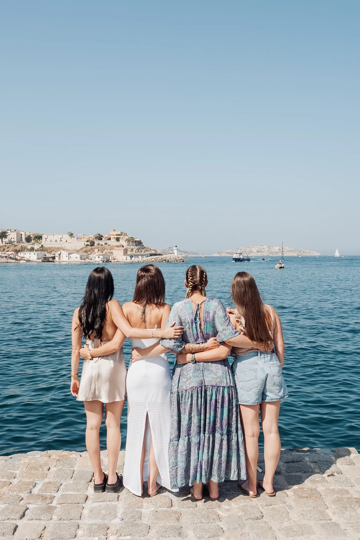 evjf-marseille-vieux-port-groupe-dos Photo EVJF à Marseille avec un petit groupe vu de dos face à la mer, bras enlacés et ambiance estivale