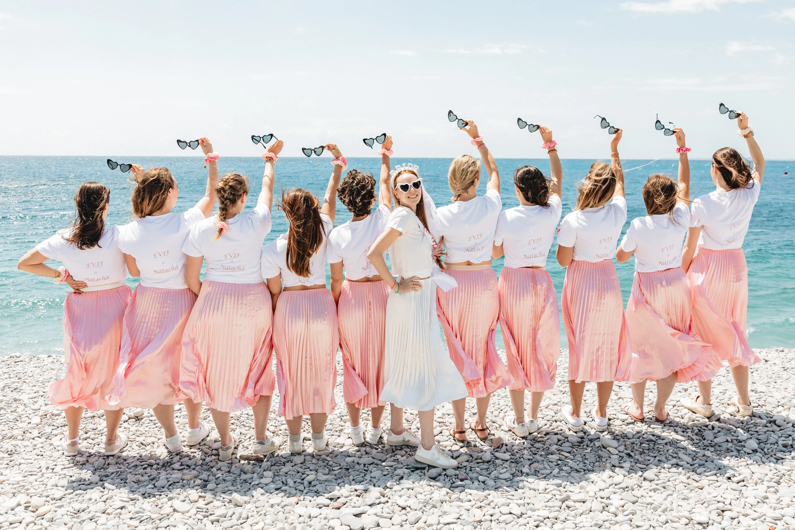 EVJF à Nice – La mariée au centre et ses amies de dos lèvent leurs lunettes cœur vers le ciel face à la mer