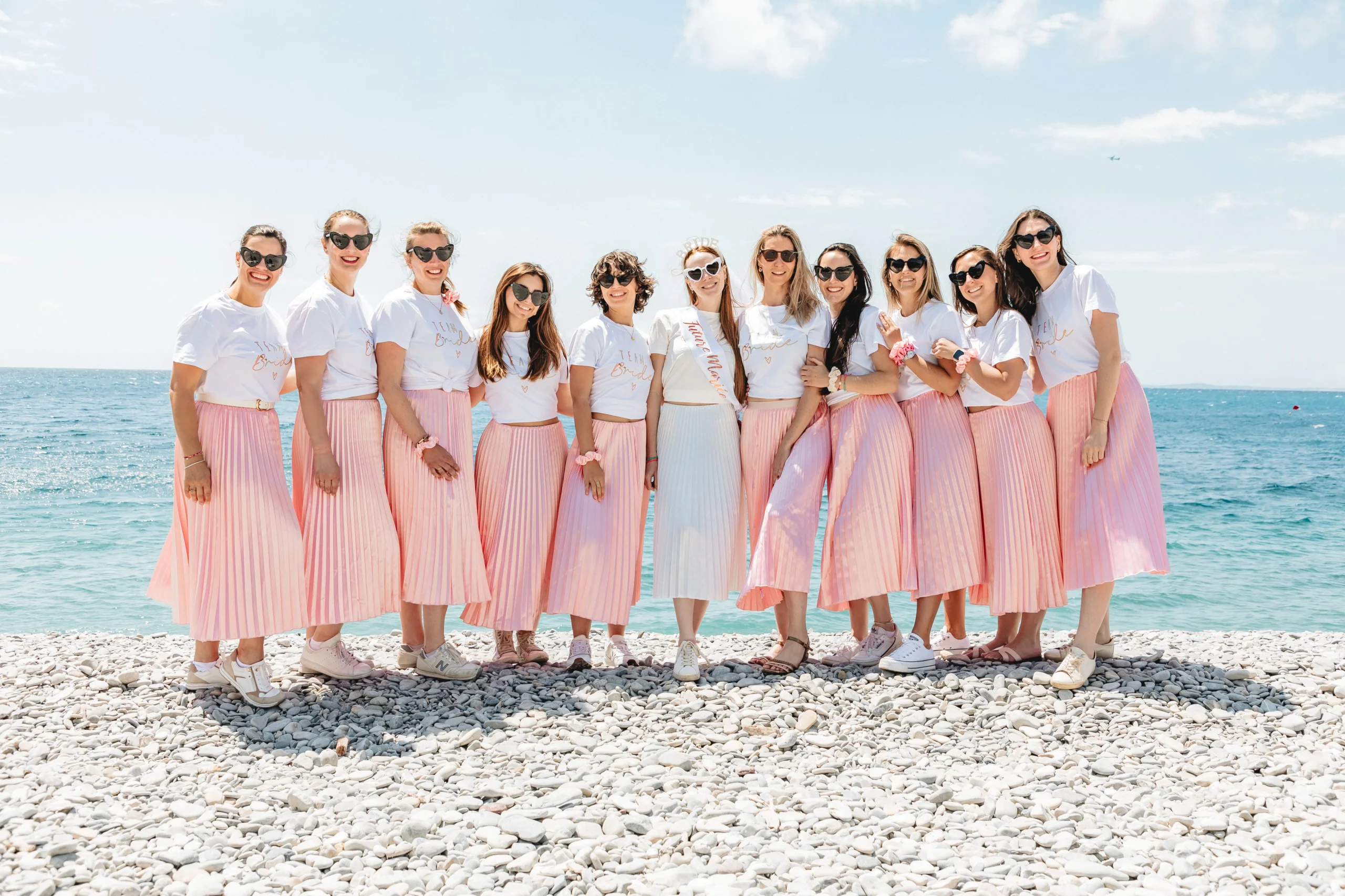 : EVJF à Nice – Photo de groupe de la team bride au complet devant la mer, toutes en harmonie rose et blanc