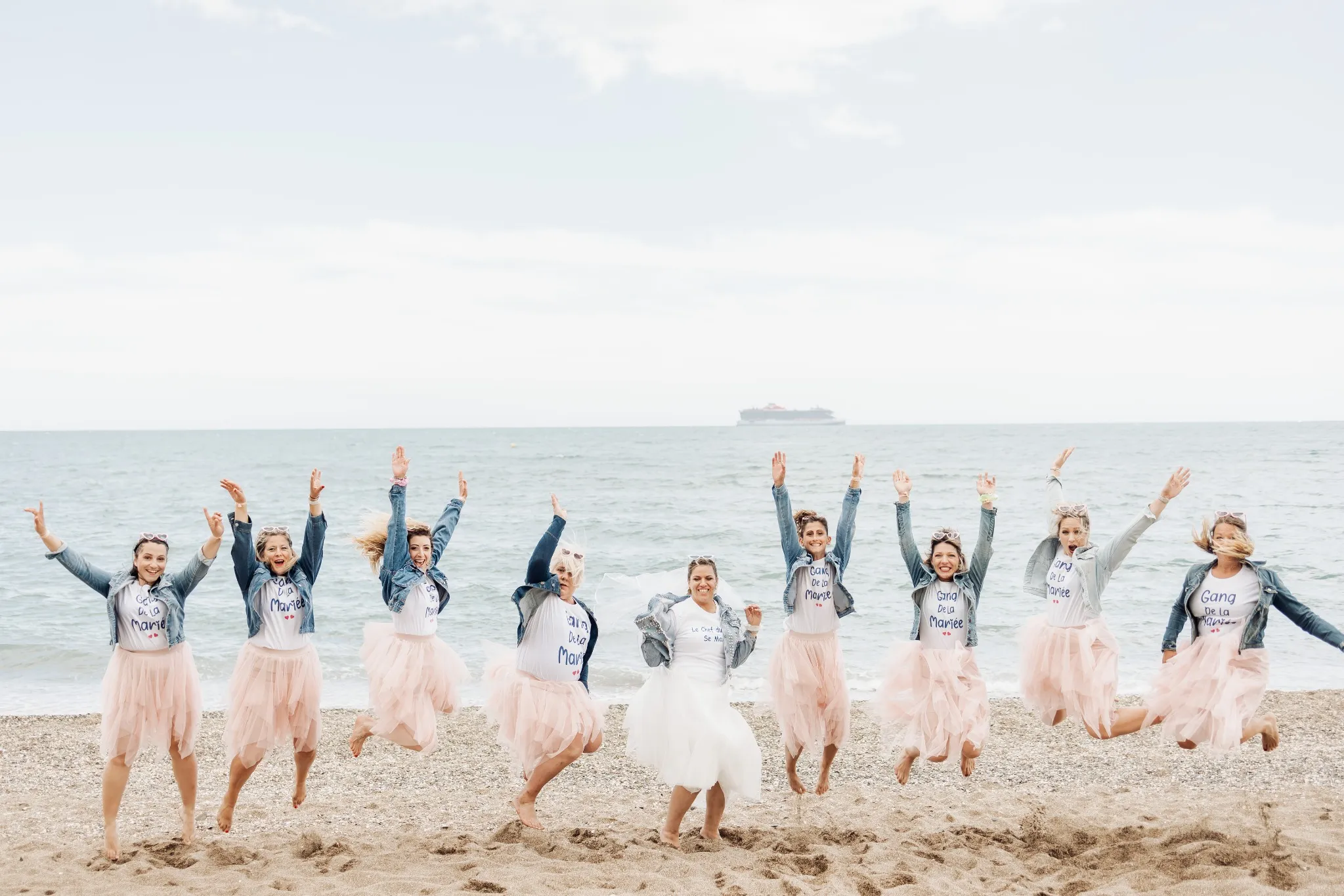 Photo de groupe EVJF sur une plage de Malaga avec toutes les participantes sautant en l'air, en tulle rose et veste en jean

