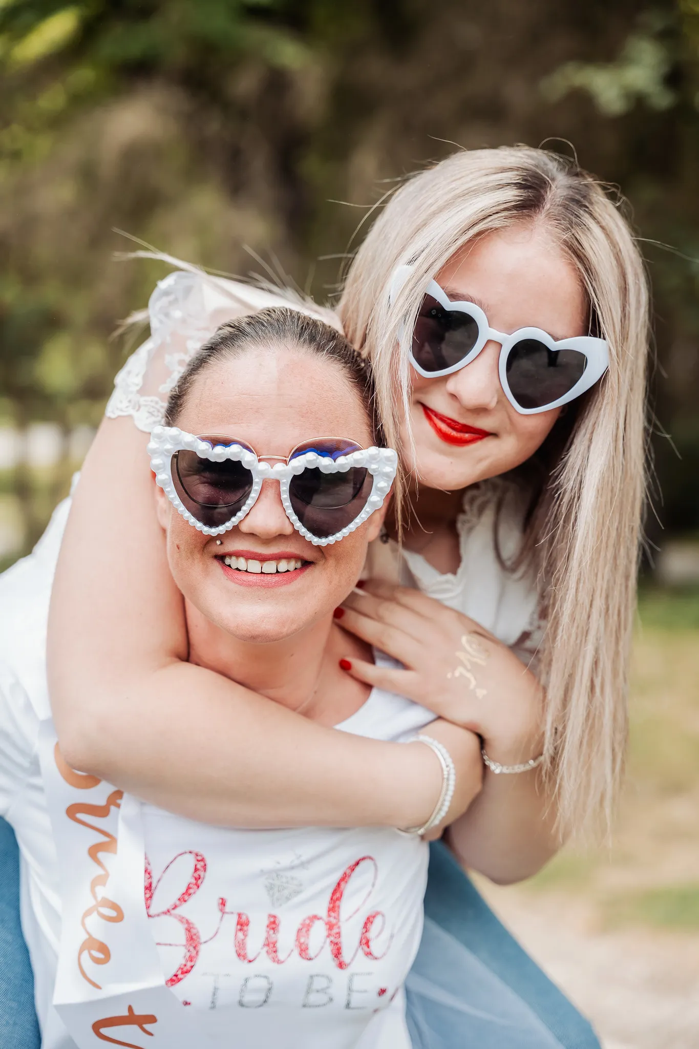 EVJF à Reims – Moment complice et câlin entre amies avec lunettes en cœur Deux femmes souriantes lors d’un EVJF à Reims, l’une portant l’autre sur son dos, toutes deux en lunettes cœur, dans une ambiance festive.