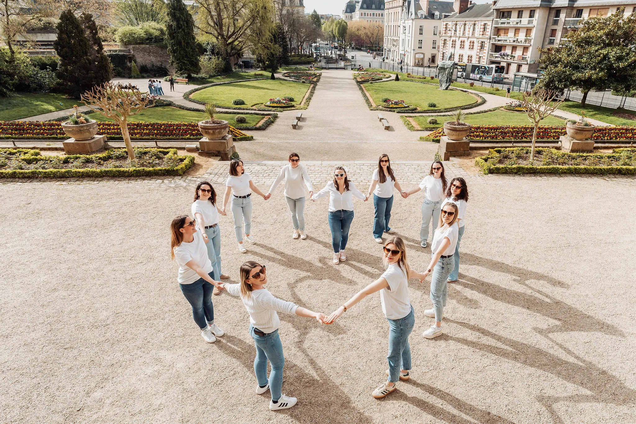 EVJF à Rennes – Cercle de femmes dans un jardin public avec tenues coordonnées Groupe de femmes formant un cercle main dans la main dans un parc au cœur de Rennes, toutes en jean et haut blanc, lors d’un EVJF.