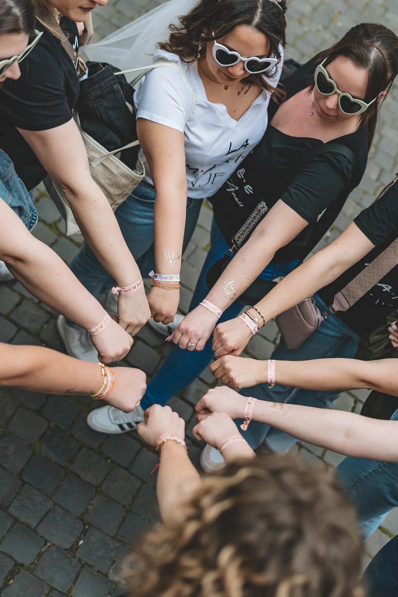 EVJF à Rome – Cercle de mains unies par les bracelets Team Bride Gros plan sur un cercle de poings fermés portant des bracelets EVJF assortis, symbolisant l’unité du groupe lors d’un EVJF à Rome.