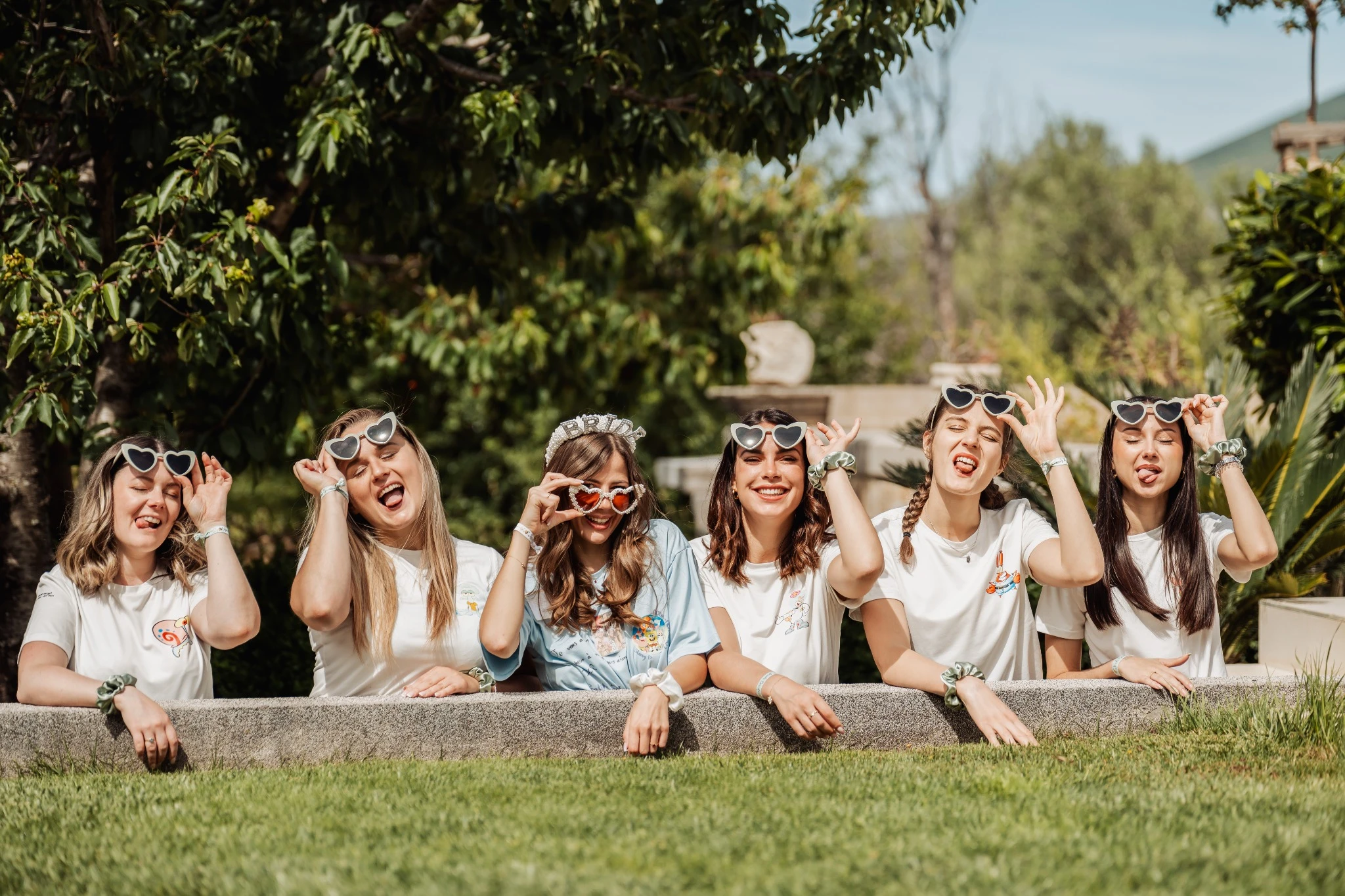 Délire entre copines pendant un EVJF à Split, les filles en lunettes cœur tirant la langue dans un jardin verdoyant.