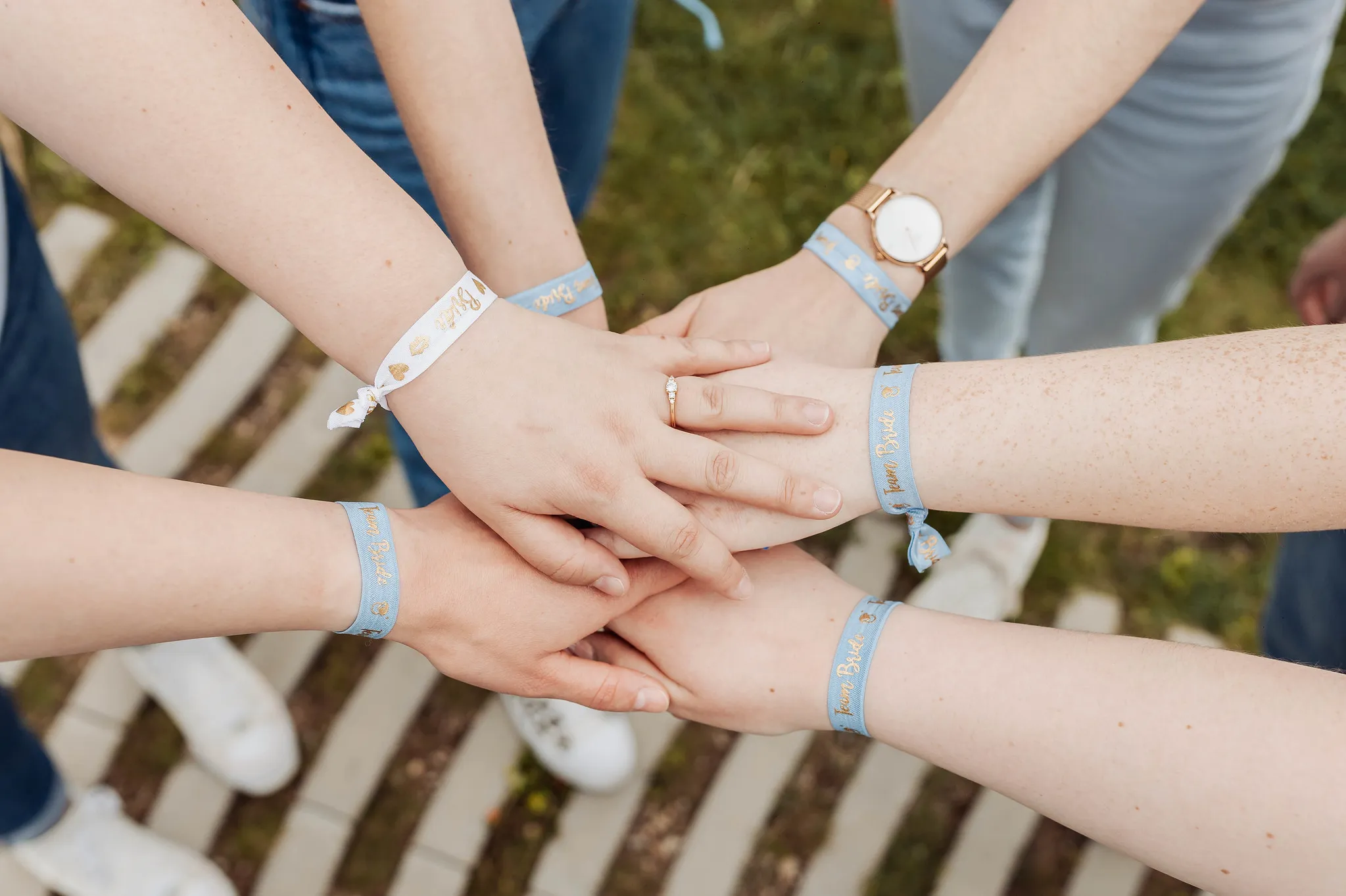 EVJF à Toulon – Mains empilées avec bracelets bleus "Team Bride" Gros plan sur des mains superposées portant des bracelets bleus "Team Bride", avec une bague de fiançailles visible au centre, pendant un EVJF à Toulon.