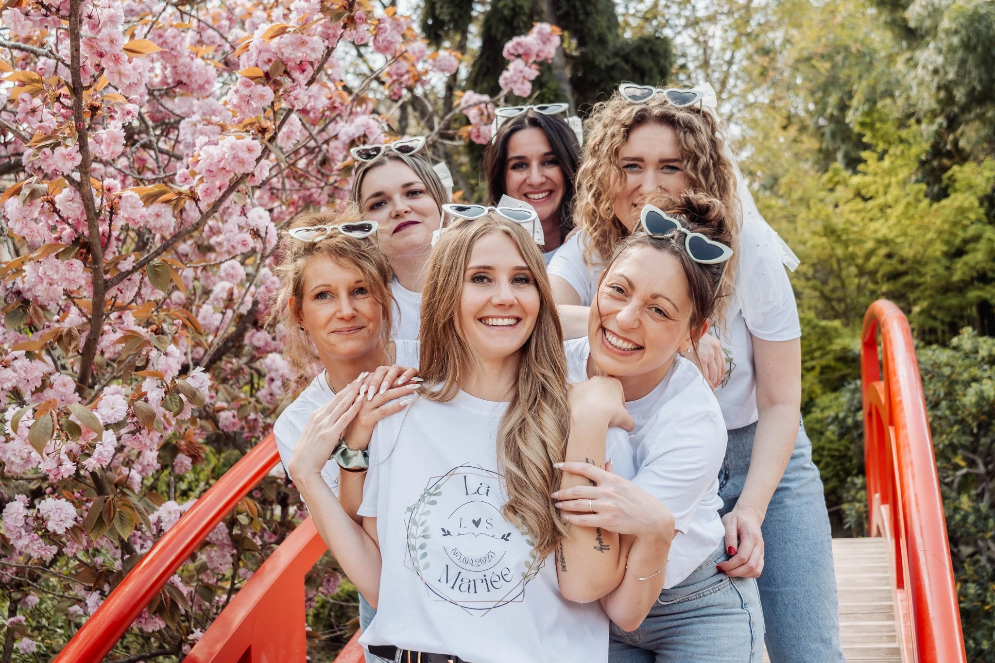 La future mariée entourée de ses amies sur un pont rouge entouré de cerisiers fleuris lors d’un EVJF à Toulouse.