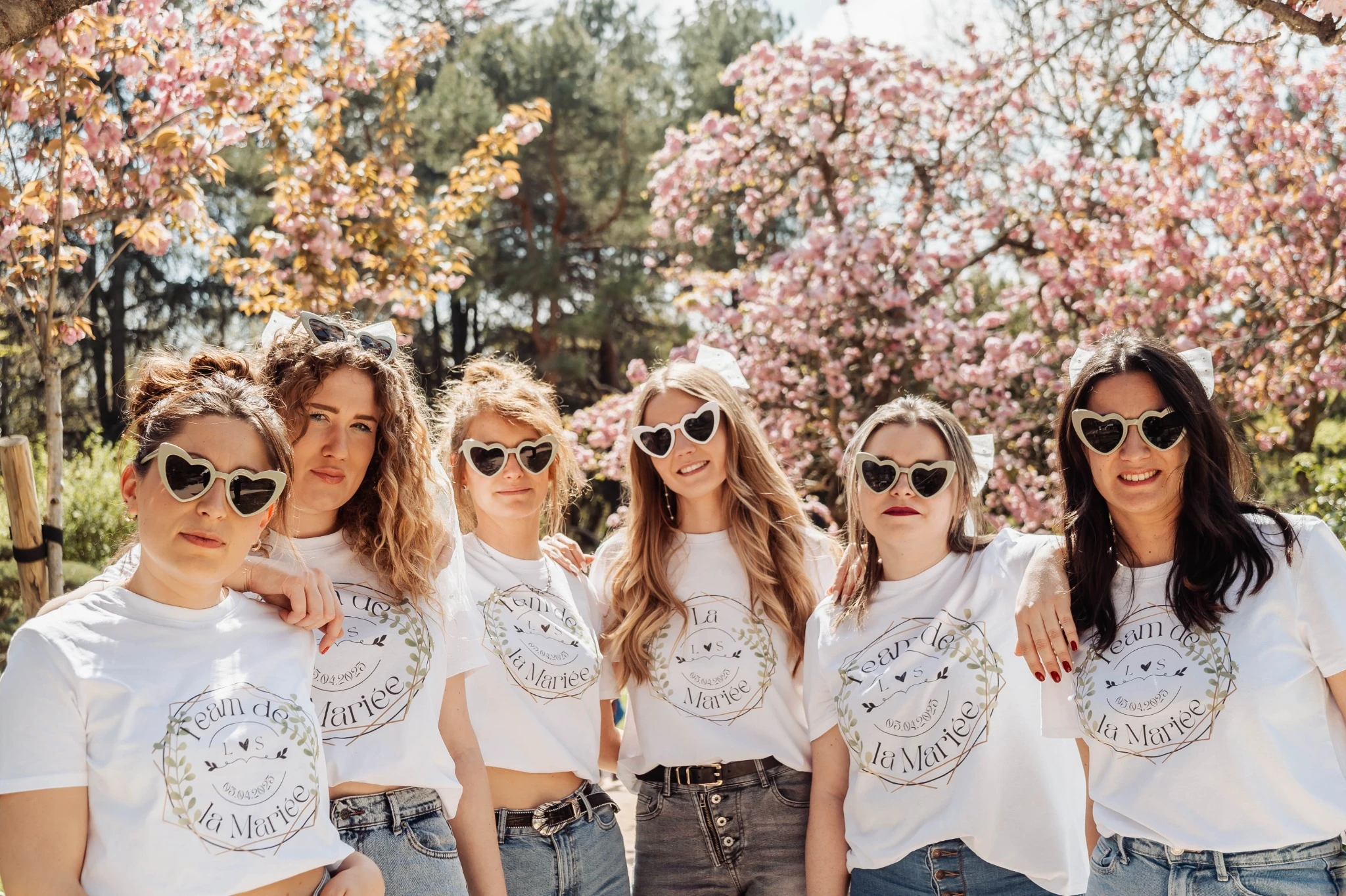 Groupe de femmes portant des t-shirts “Team de la Mariée” et des lunettes cœur, posant sous des cerisiers en fleurs lors d’un EVJF à Toulouse.