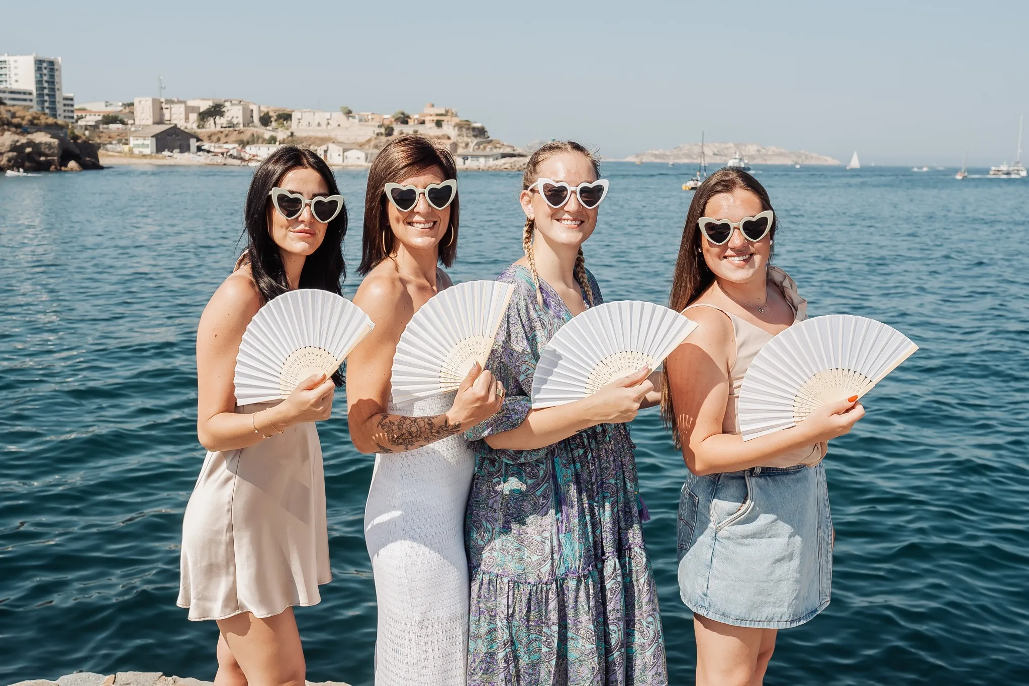 Portrait EVJF à Marseille avec éventails et lunettes cœur face à la mer, tenues d’été stylées