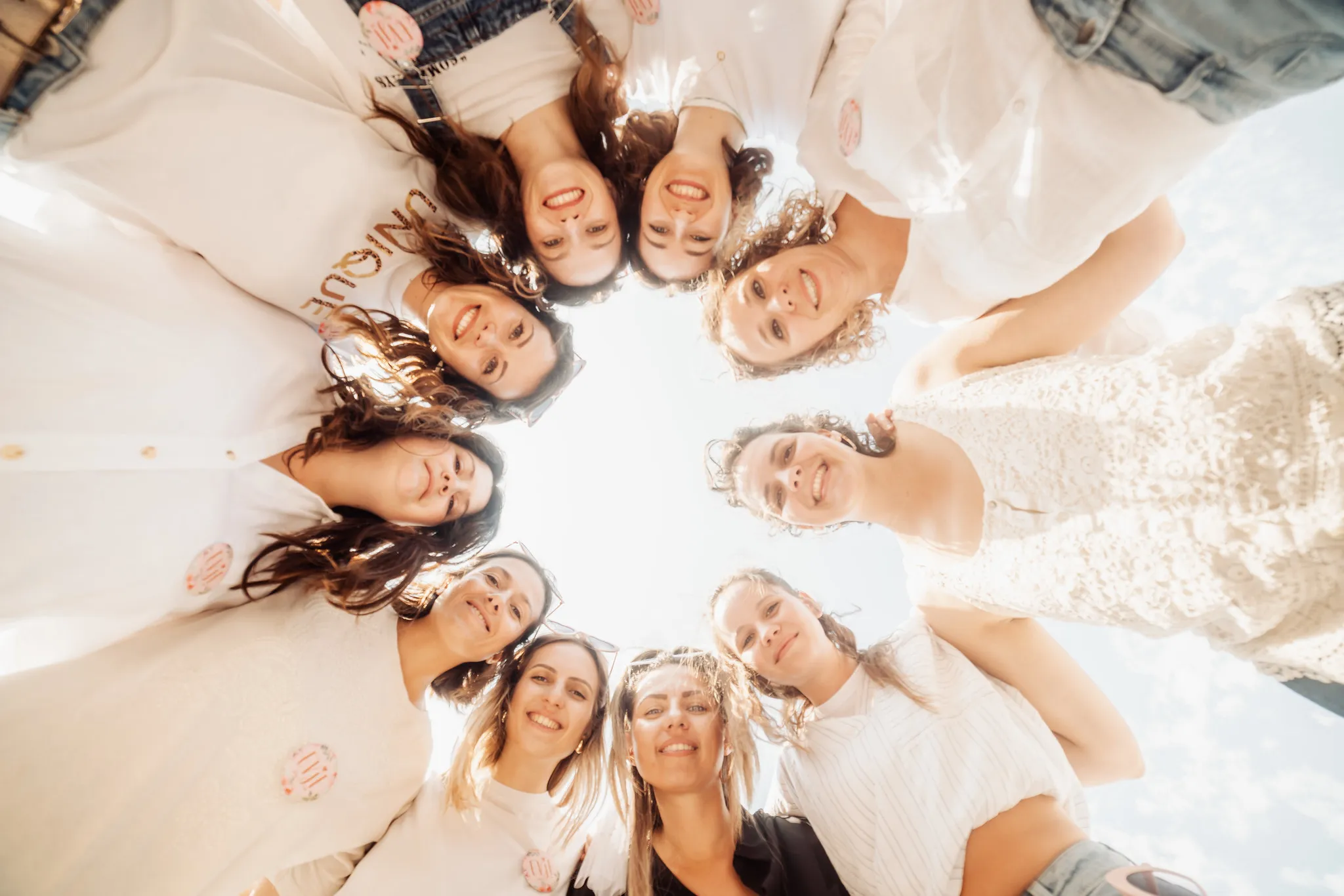 Photo de groupe EVJF à Marseille – Femmes souriantes sous le soleil du Sud Photo d’un groupe de femmes réunies en cercle pour un EVJF à Marseille, souriantes et joyeuses sous un ciel bleu, prises en contre-plongée.