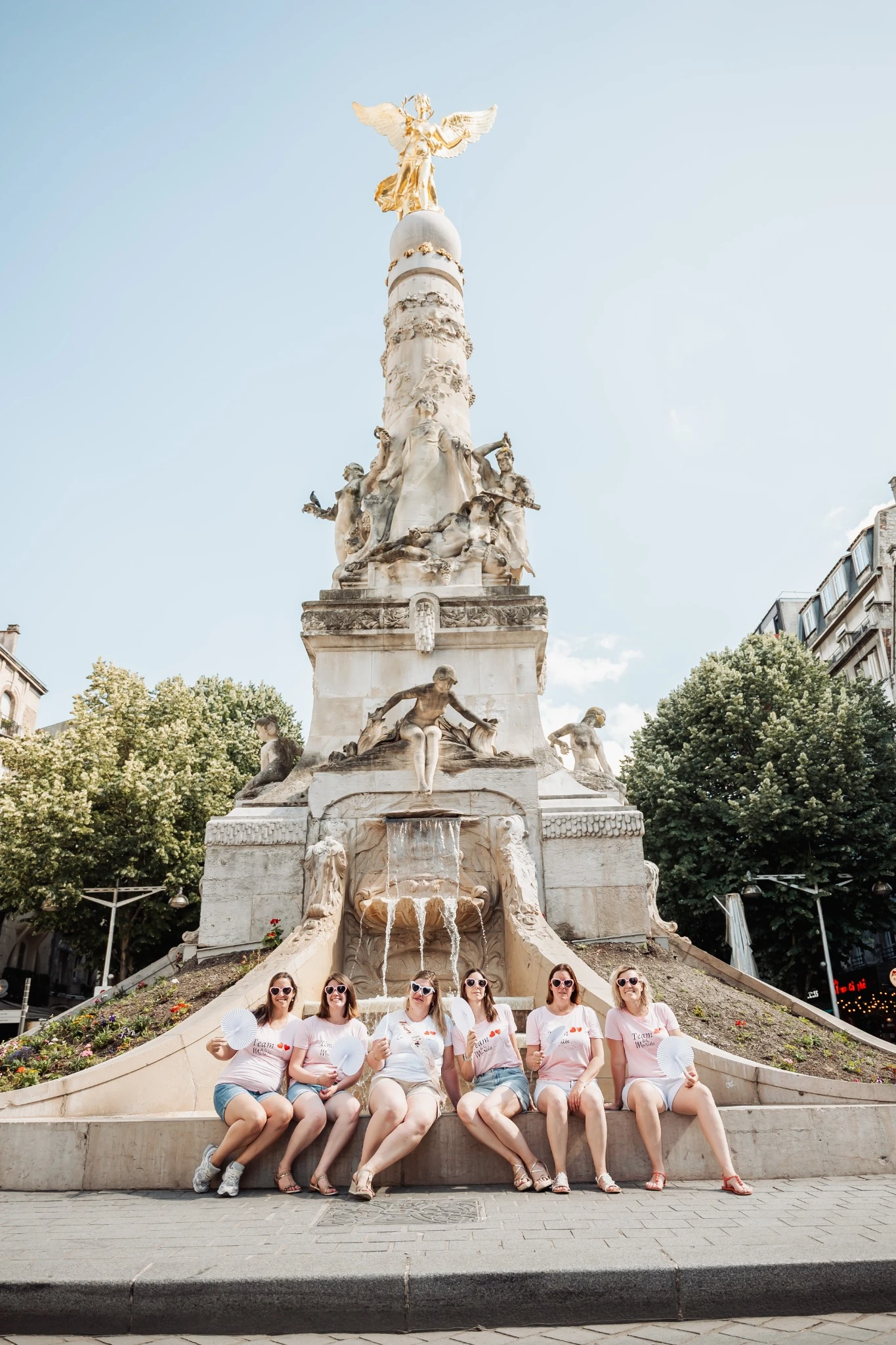 photos-evjf-reims-fontaine-ange-place-royale Groupe de femmes en EVJF à Reims posant devant la fontaine de la place Royale avec l'ange doré
