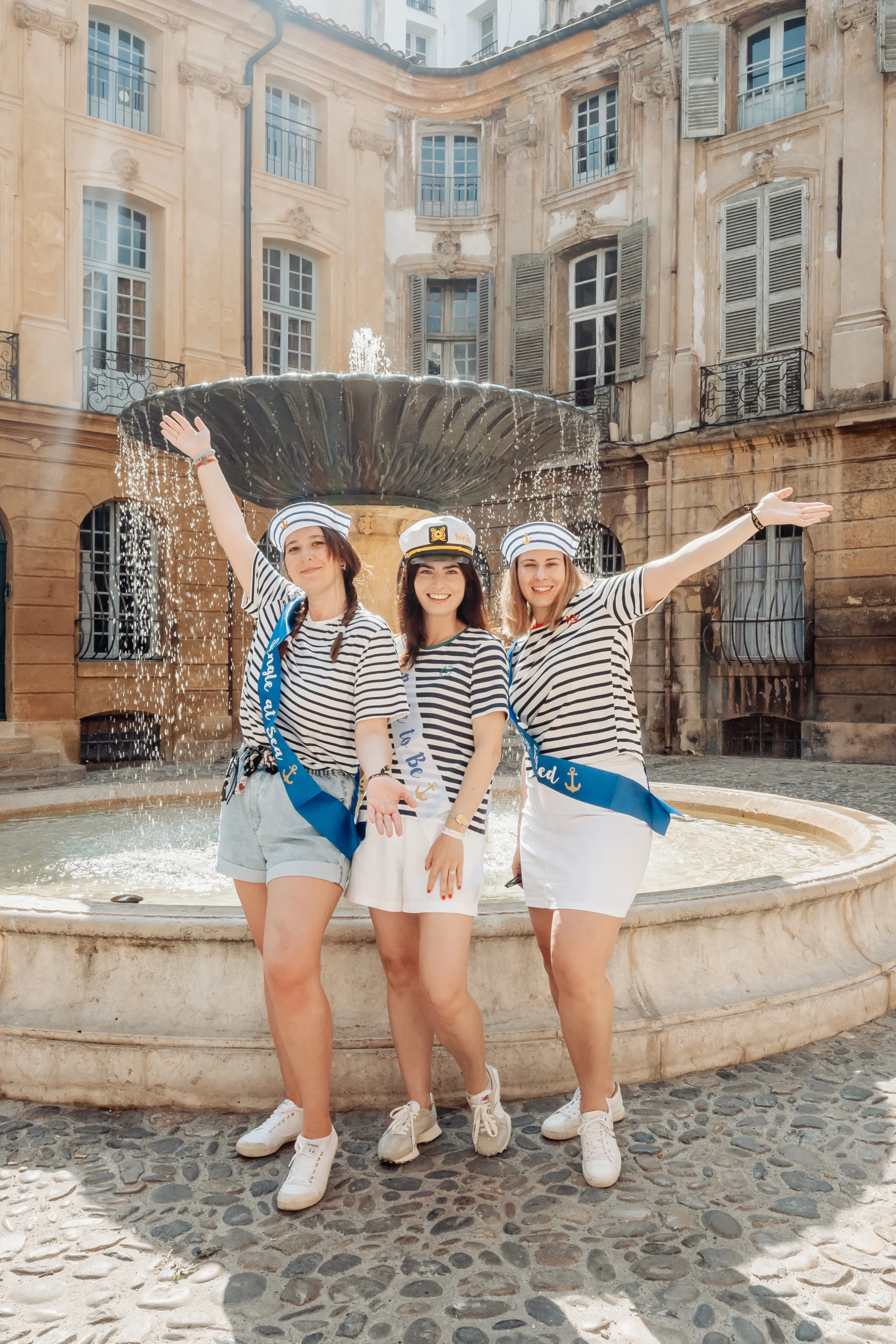 shooting-evjf-aix-en-provence-fontaine-maison-nationale Photo EVJF à Aix-en-Provence devant une fontaine historique, avec des amies en marinière et chapeaux de marin, ambiance festive et ensoleillée