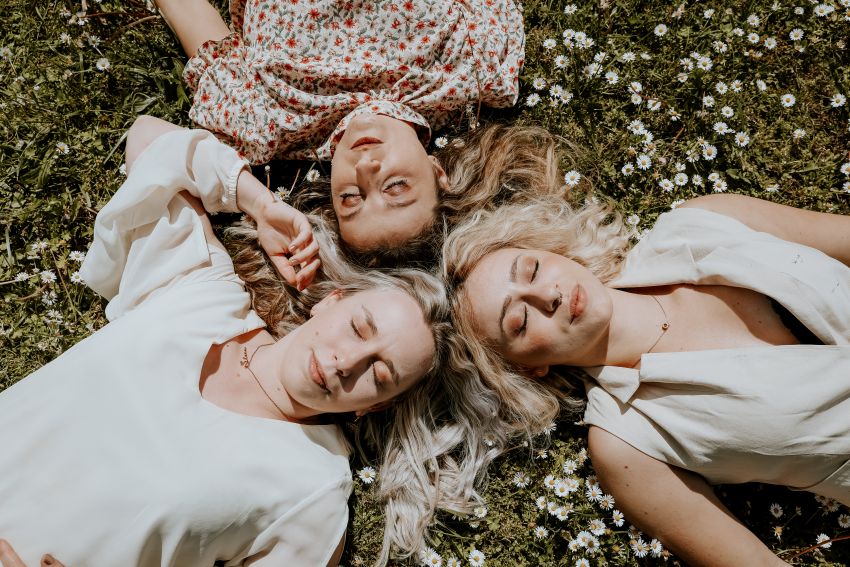 trois filles qui posent allongées dans l'herbe au milieu des fleures